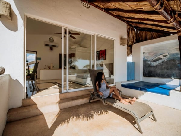 Terraza con palapa y camastro junto a la entrada de la recámara principal, con arte mural y asientos azules