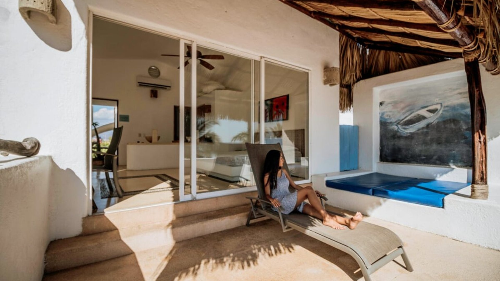 Terraza con palapa y camastro junto a la entrada de la recámara principal, con arte mural y asientos azules