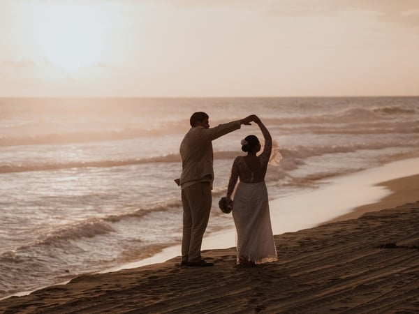 Pareja de novios bailando en la playa al atardecer frente al mar Pacífico con luz dorada