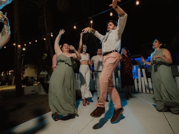 Invitados celebrando en pista de baile nocturna con luces colgantes y palmeras de fondo