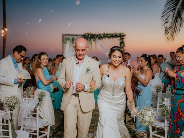 Ceremonia de boda al atardecer frente al océano con arco floral y sillas blancas decoradas