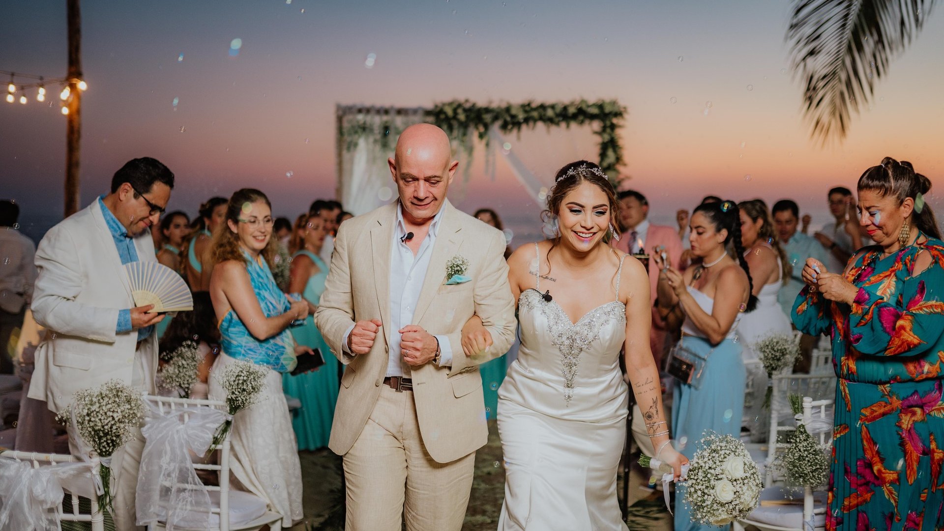 Ceremonia de boda al atardecer frente al océano con arco floral y sillas blancas decoradas