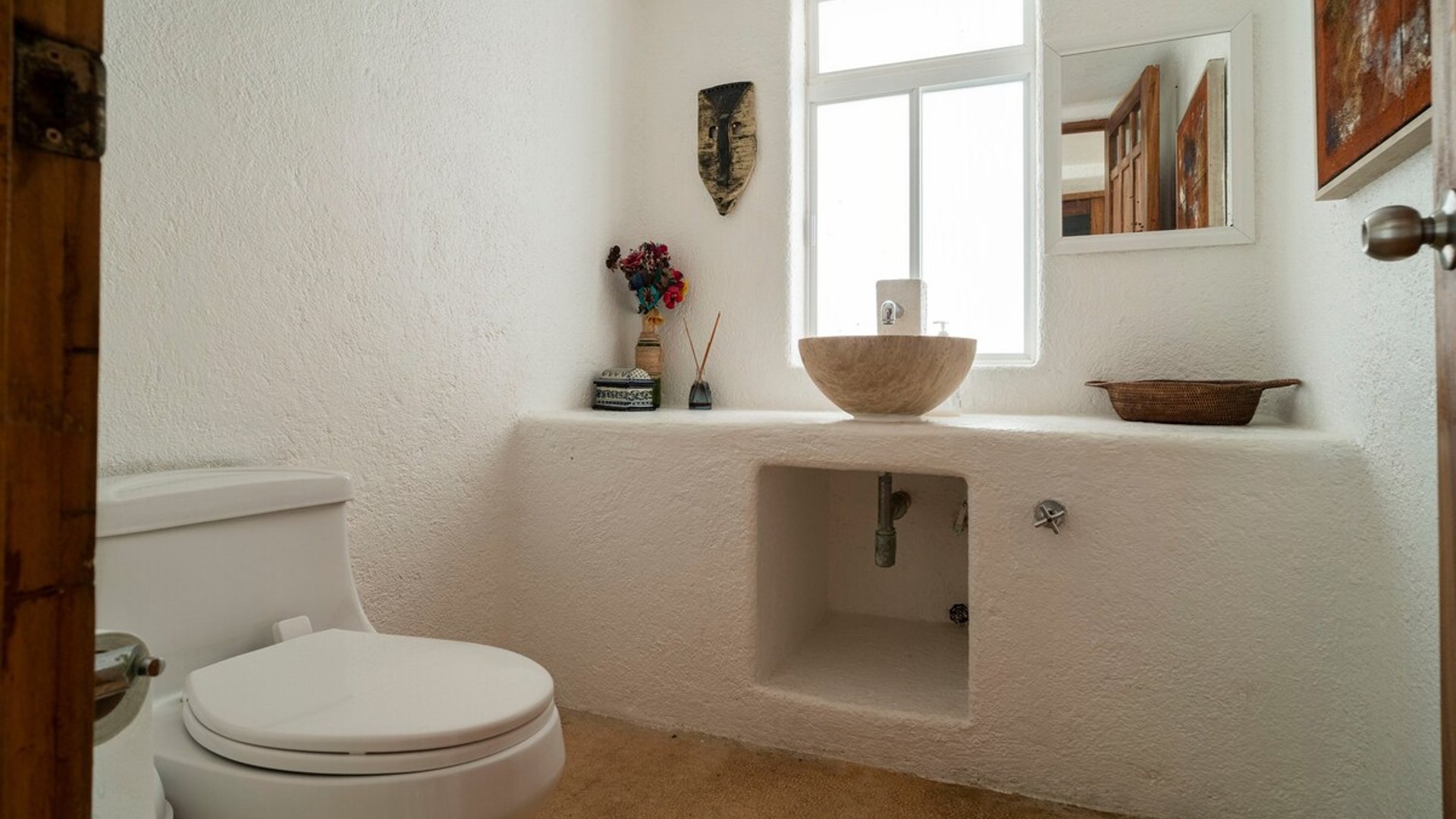 Baño blanco con lavabo de piedra sobre cubierta de mampostería, ventana cenital y detalles artesanales