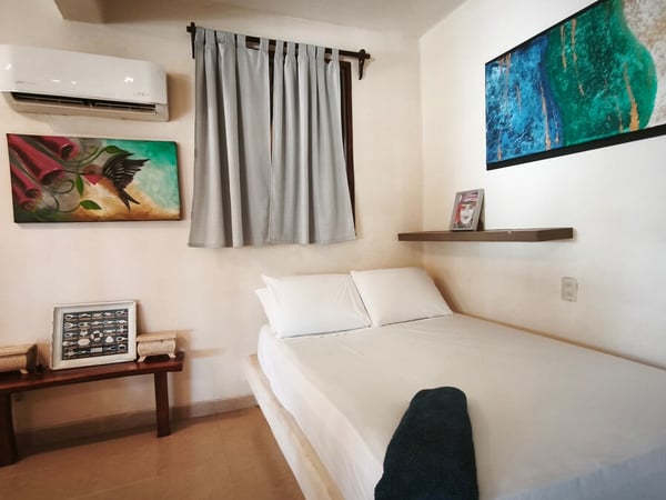 Recámara compacta con cama doble, cuadros de arte coloridos y clima de pared en tono blanco cálido