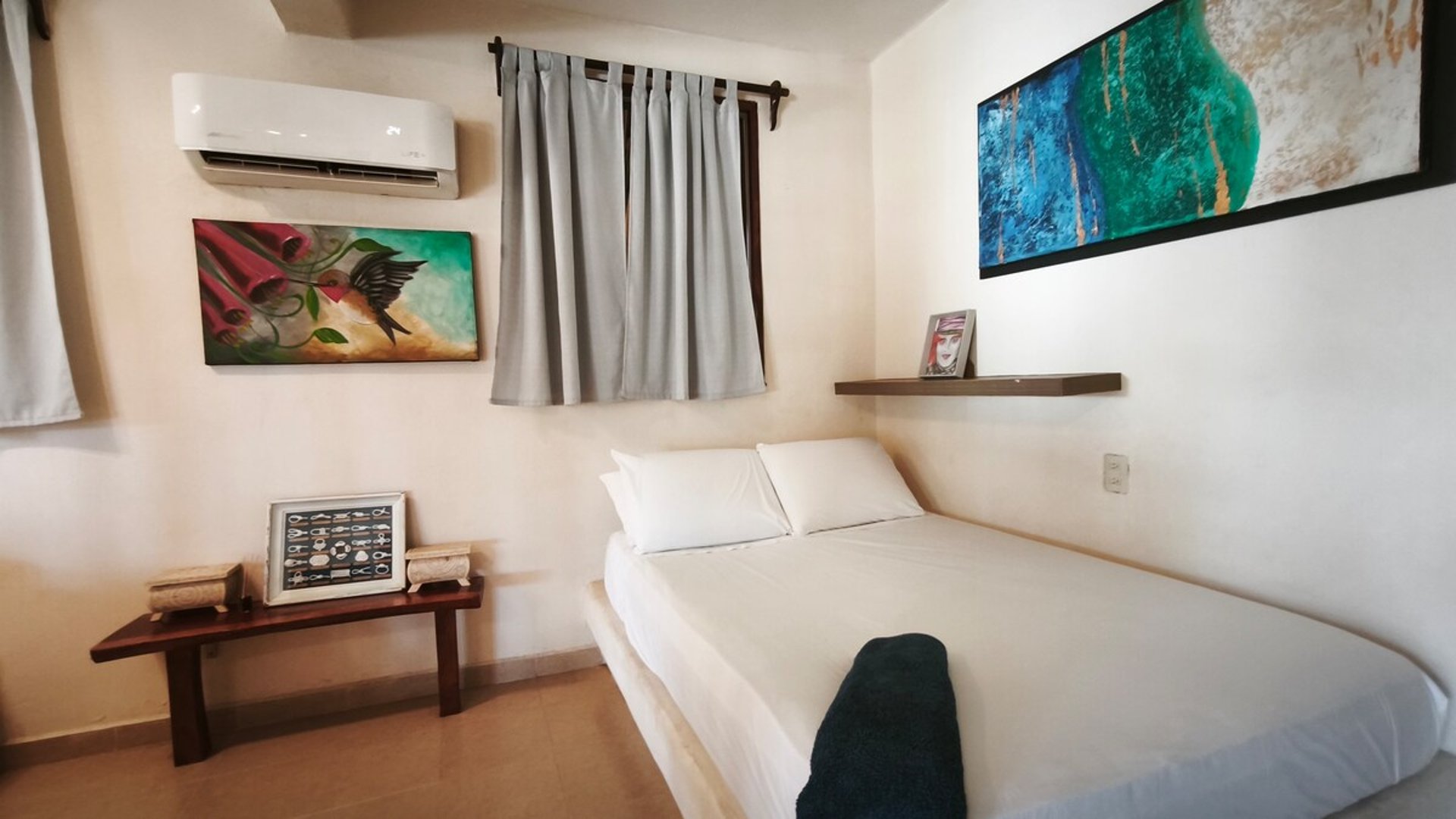 Recámara compacta con cama doble, cuadros de arte coloridos y clima de pared en tono blanco cálido