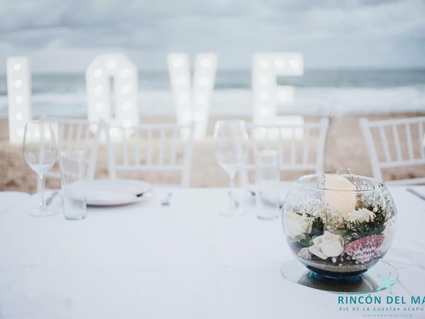 Centro de mesa floral en boda de playa con letras LOVE iluminadas y el mar al fondo