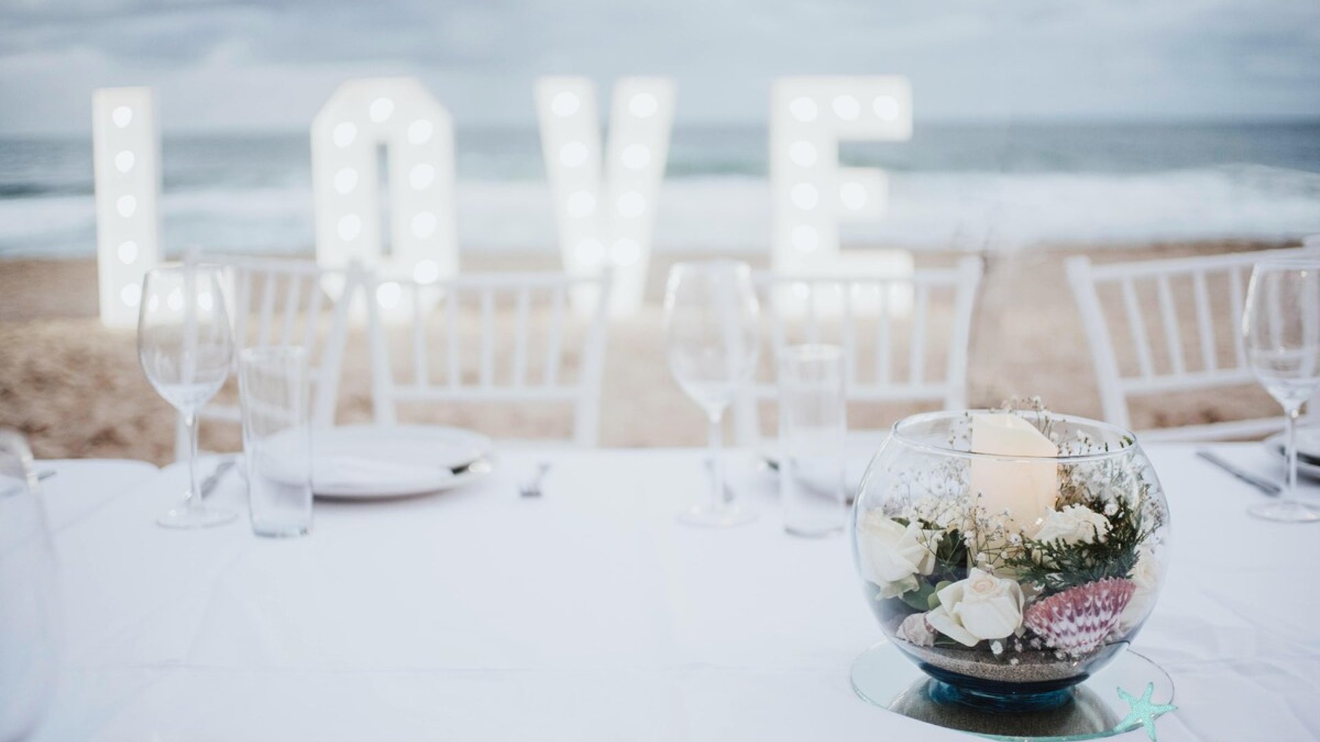 Centro de mesa floral en boda de playa con letras LOVE iluminadas y el mar al fondo