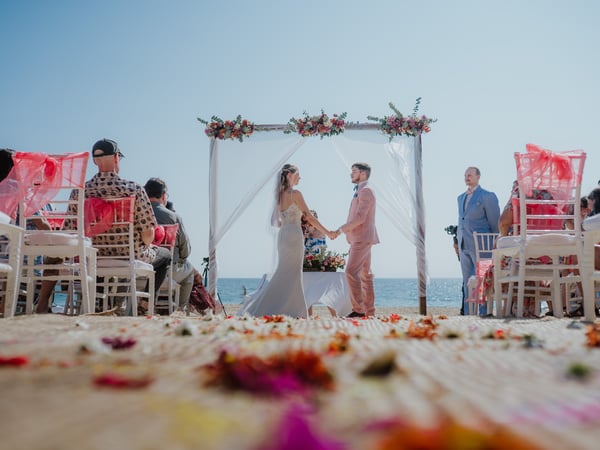 Ceremonia de boda en playa con arco floral y sillas decoradas frente al mar bajo cielo despejado
