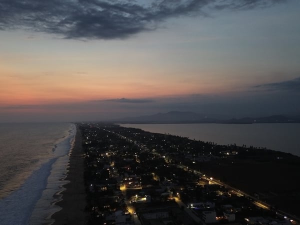 Vista aérea al atardecer de la franja costera de Pie de la Cuesta, con el Pacífico al oeste y la laguna al este bajo cielo rosado