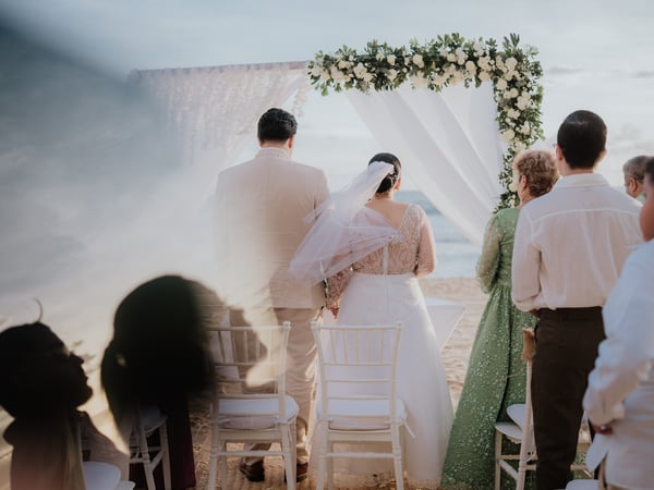 Ceremonia de boda frente al mar con arco floral blanco y telas ondeando con brisa costera