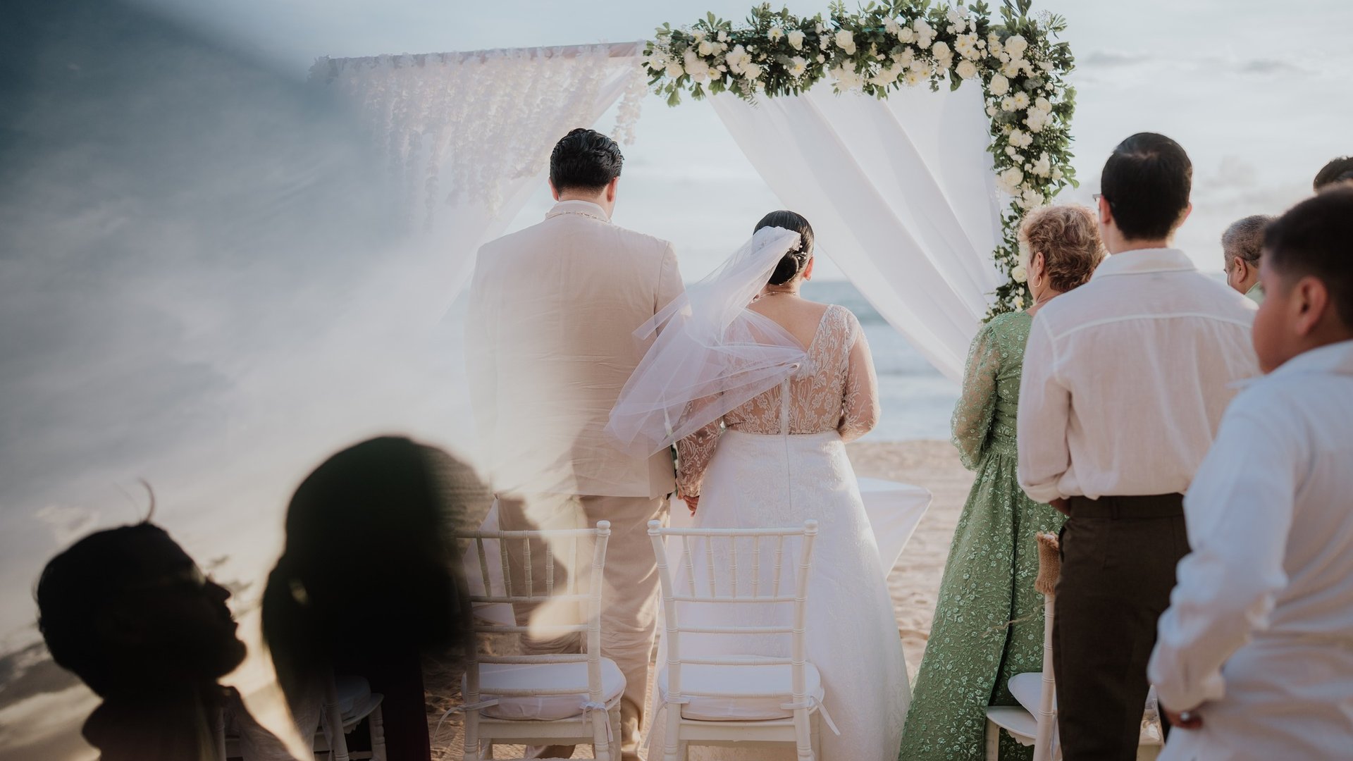 Ceremonia de boda frente al mar con arco floral blanco y telas ondeando con brisa costera