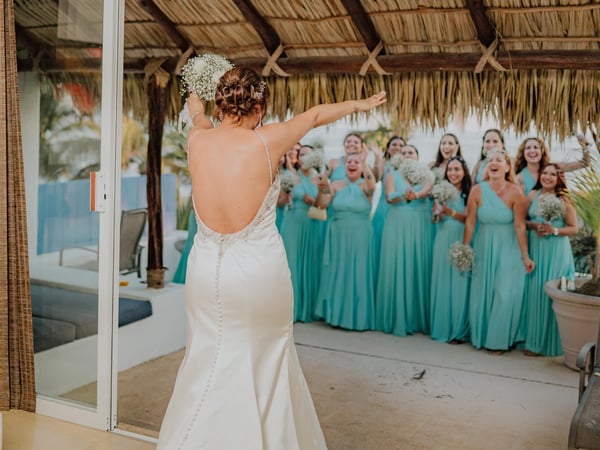 Lanzamiento de ramo bajo palapa frente a damas de honor con vestidos turquesa y alberca