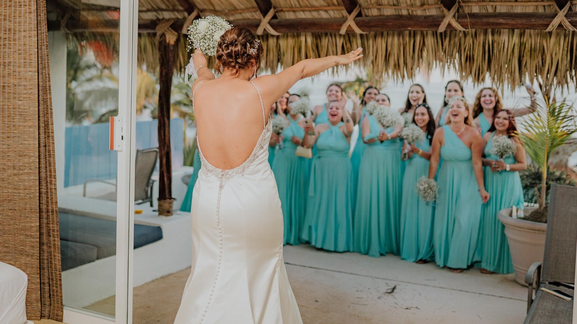 Lanzamiento de ramo bajo palapa frente a damas de honor con vestidos turquesa y alberca