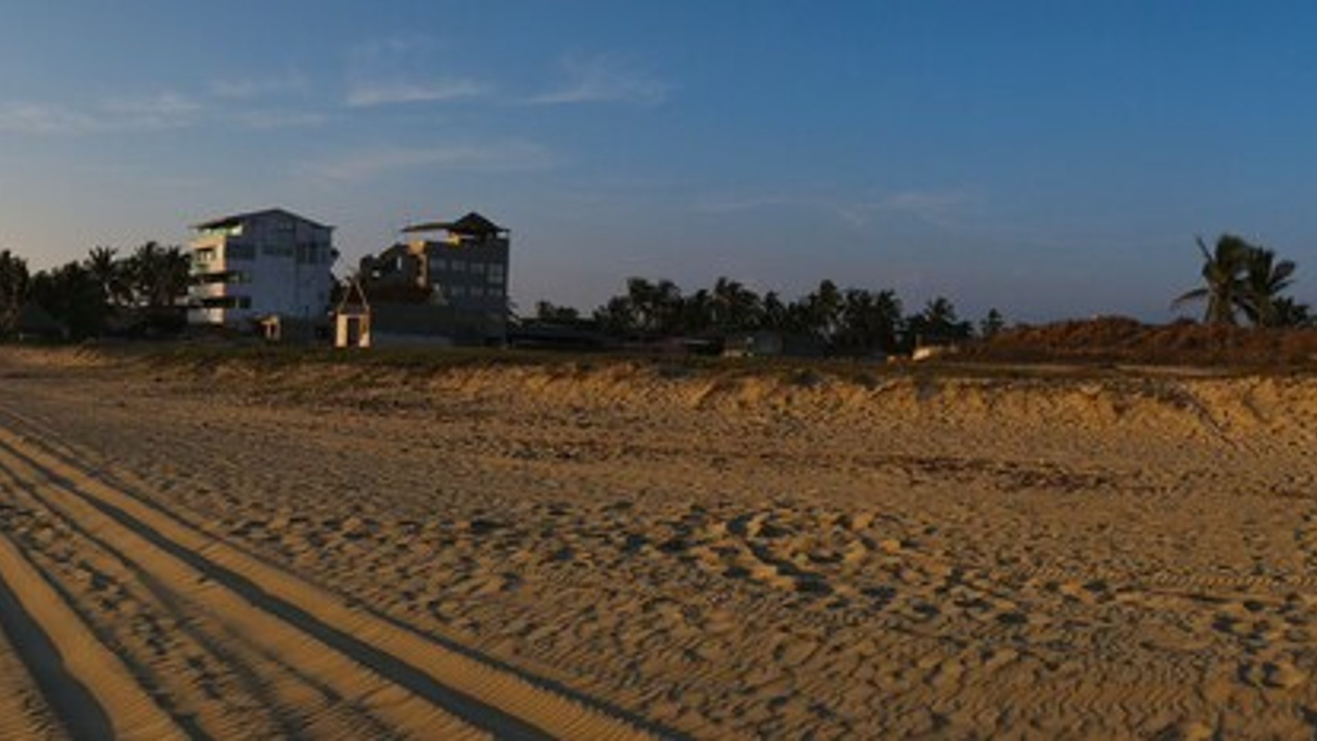 Vista panorámica de playa amplia al atardecer con propiedades frente al mar y palmeras al fondo
