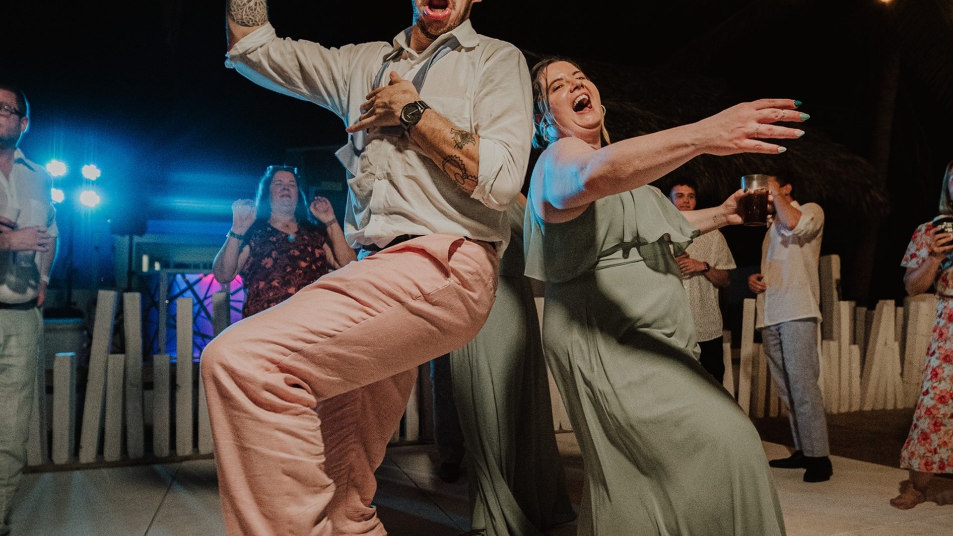Invitados bailando en pista nocturna de boda con luces colgantes y ambiente festivo tropical
