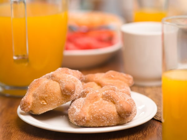 Desayuno mexicano con pan dulce azucarado, jugo de naranja, fruta fresca y huevos sobre mesa de madera