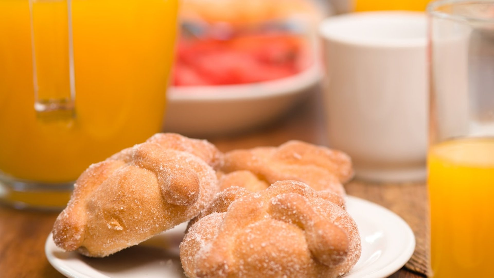 Desayuno mexicano con pan dulce azucarado, jugo de naranja, fruta fresca y huevos sobre mesa de madera