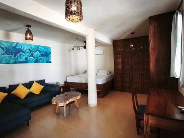 Habitación amplia con sofá azul, cama individual, muebles de madera oscura y cuadro marino en tonos turquesa