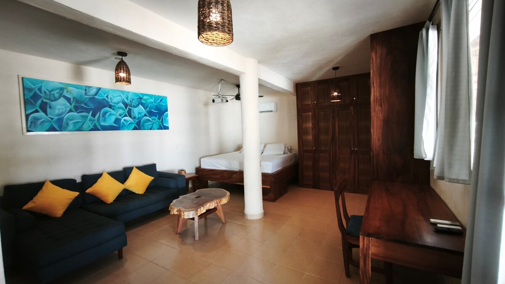 Habitación amplia con sofá azul, cama individual, muebles de madera oscura y cuadro marino en tonos turquesa