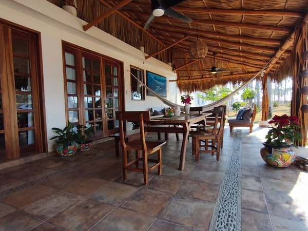 Terraza con palapa, mesa de madera, hamaca y macetas talavera frente a jardín con palmeras al fondo
