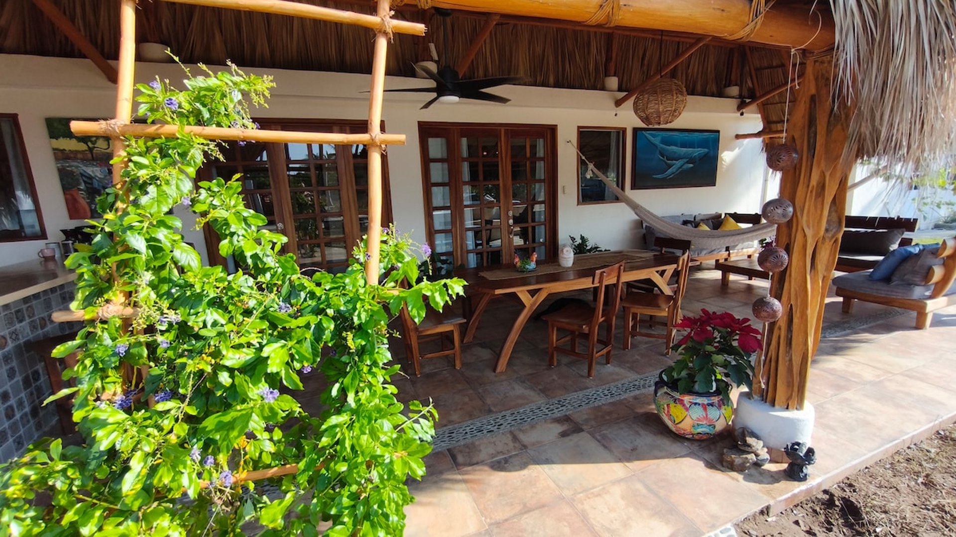 Terraza bajo palapa con comedor de madera, hamaca, vegetación trepadora y decoración artesanal mexicana