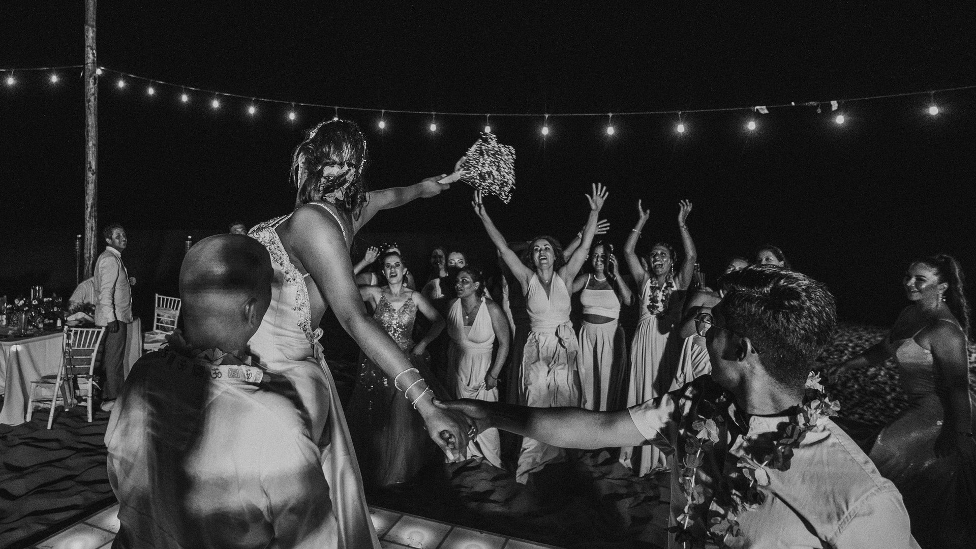 Lanzamiento de ramo en recepción nocturna con luces colgantes e invitadas en pista de baile