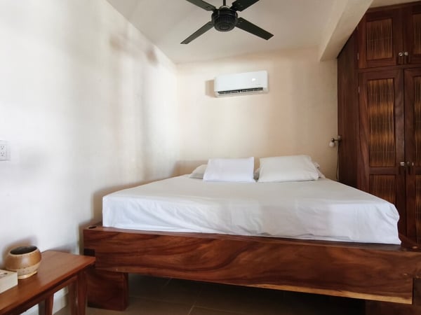 Recámara con cama doble en madera maciza, clóset de madera oscura, aire acondicionado y ventilador de techo