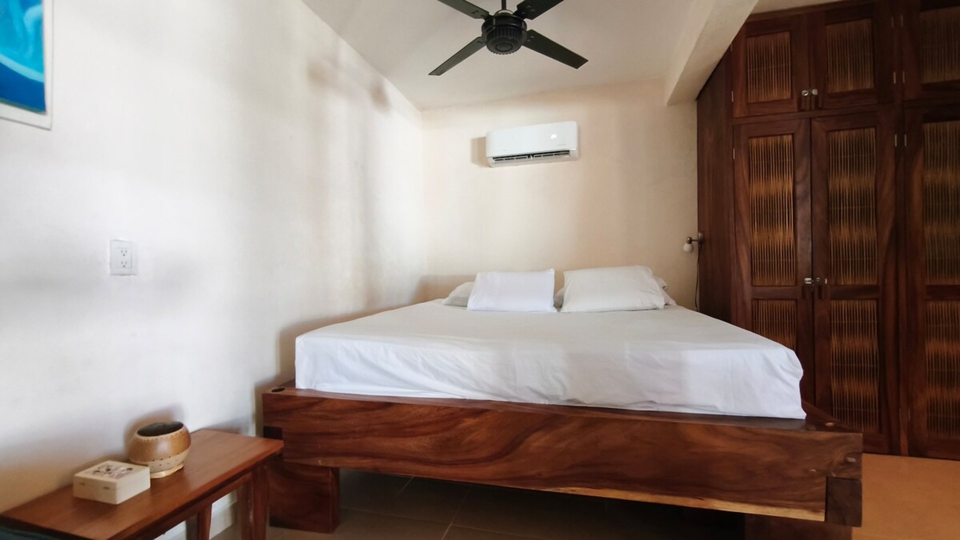 Recámara con cama doble en madera maciza, clóset de madera oscura, aire acondicionado y ventilador de techo