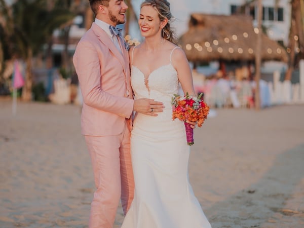 Boda en playa frente a villa con palmeras y palapa iluminada al atardecer en Pie de la Cuesta