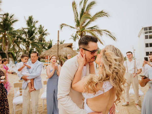 Ceremonia de boda en playa con palmeras, palapas y sillas blancas decorativas al aire libre