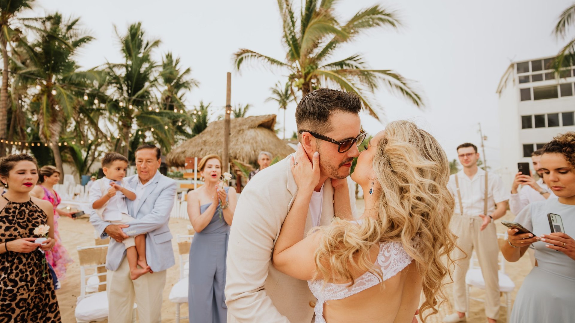 Ceremonia de boda en playa con palmeras, palapas y sillas blancas decorativas al aire libre