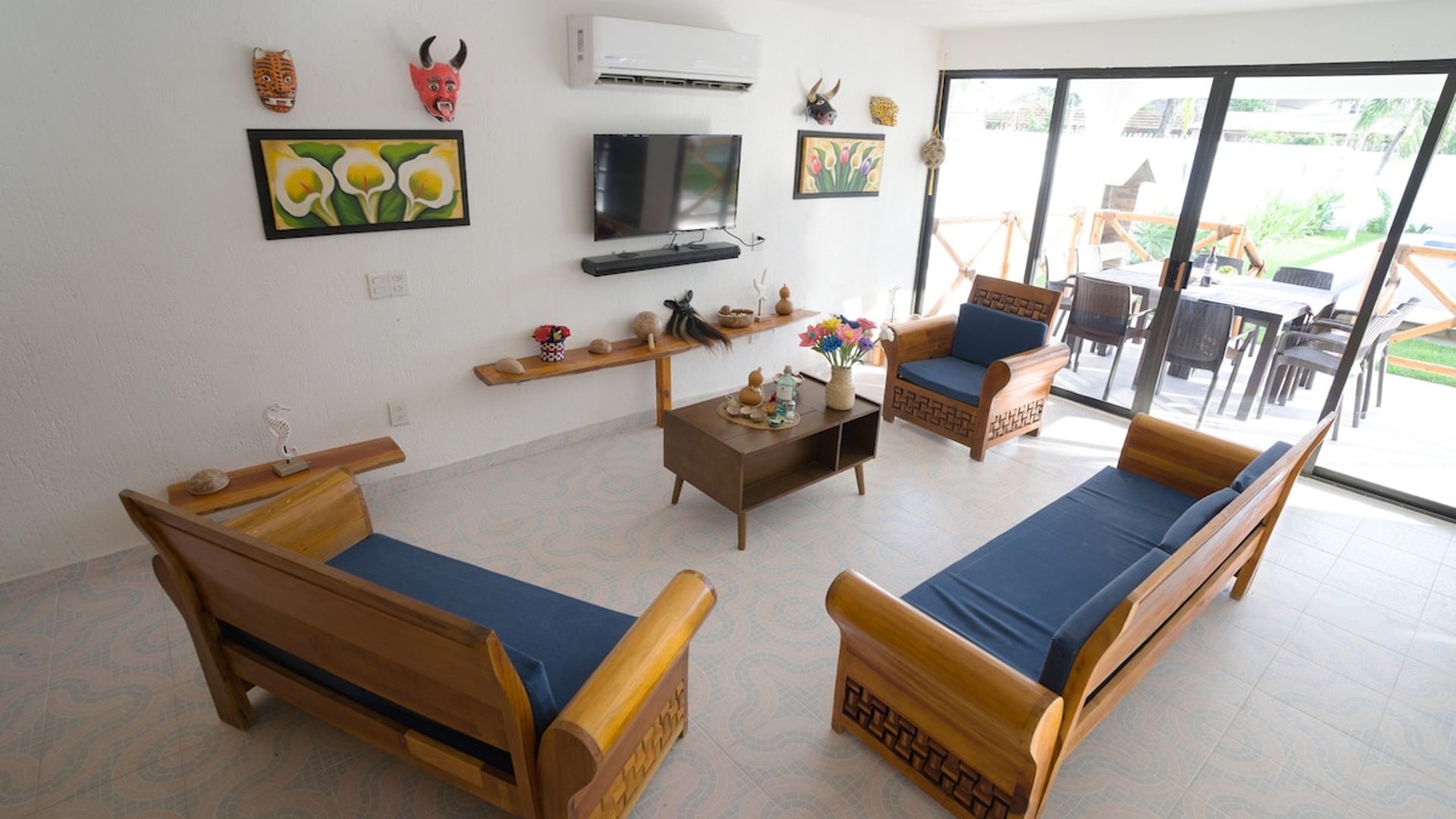 Sala amplia con muebles de madera y cojines azules, decoración artesanal en paredes y acceso a terraza exterior