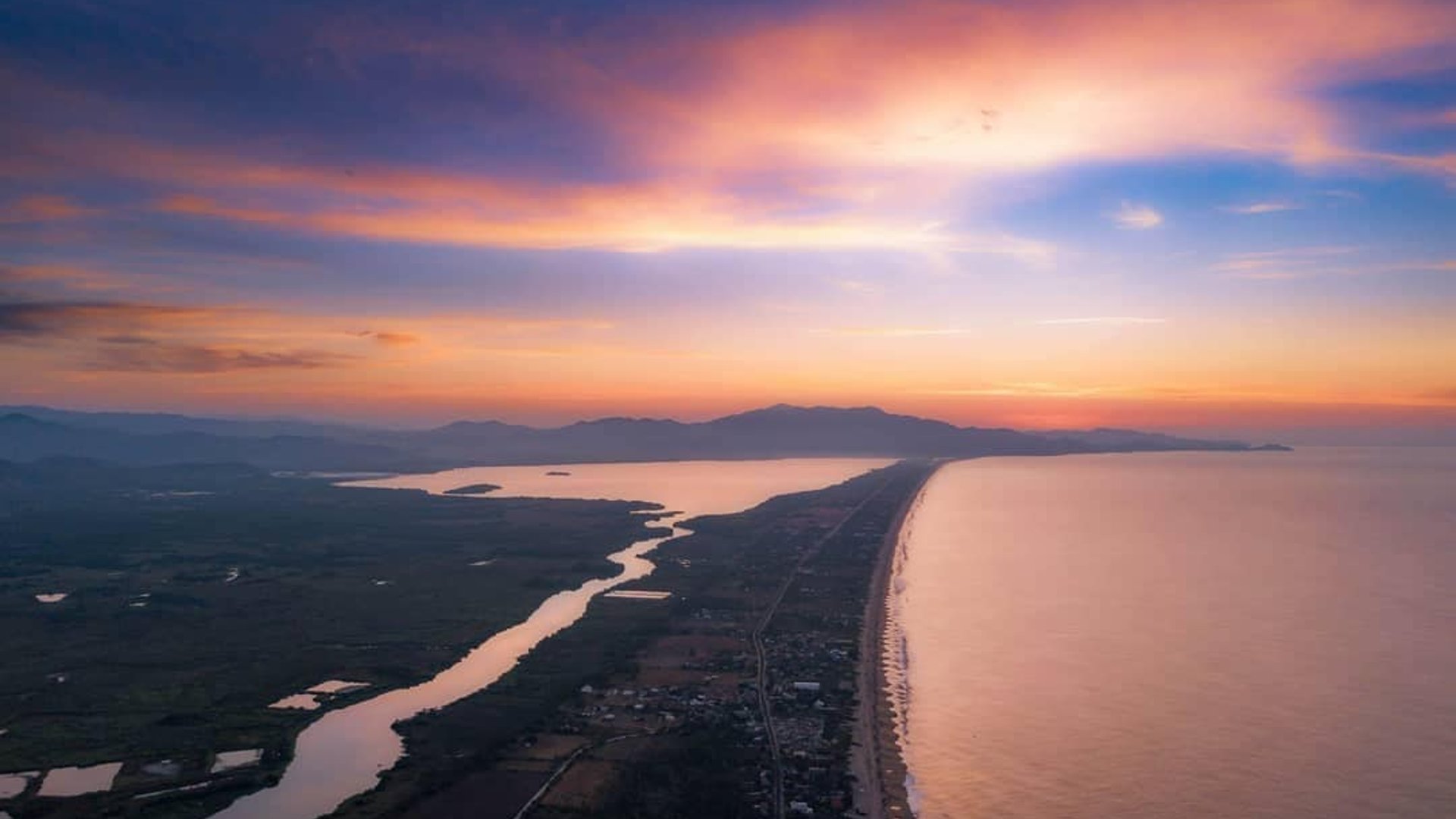 Vista aérea al atardecer de la franja costera de Pie de la Cuesta con laguna, playa y cielo en tonos naranja y violeta