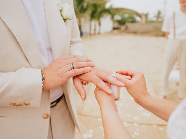 Intercambio de anillos en ceremonia de boda frente a playa con palmeras tropicales