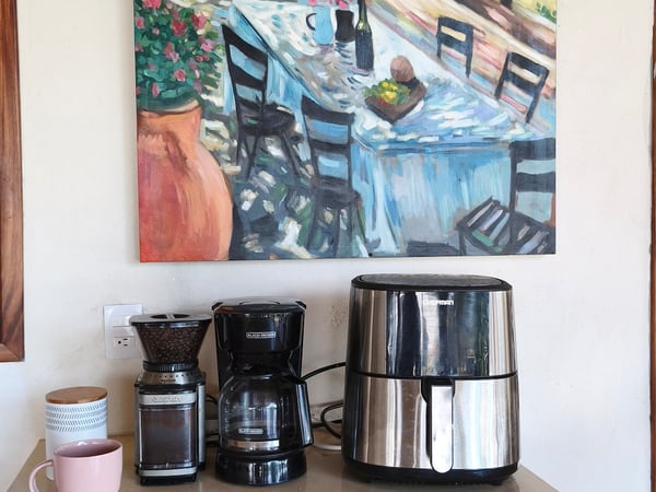 Encimera de cocina con cafetera, molino y freidora de aire junto a cuadro colorido al óleo