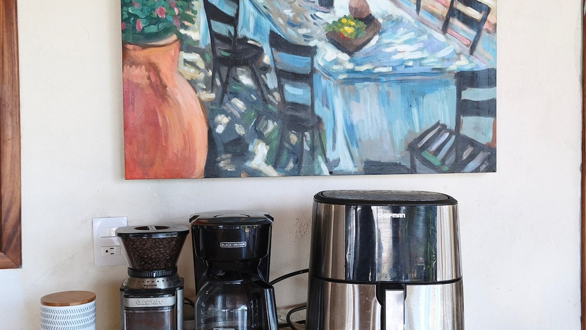 Encimera de cocina con cafetera, molino y freidora de aire junto a cuadro colorido al óleo
