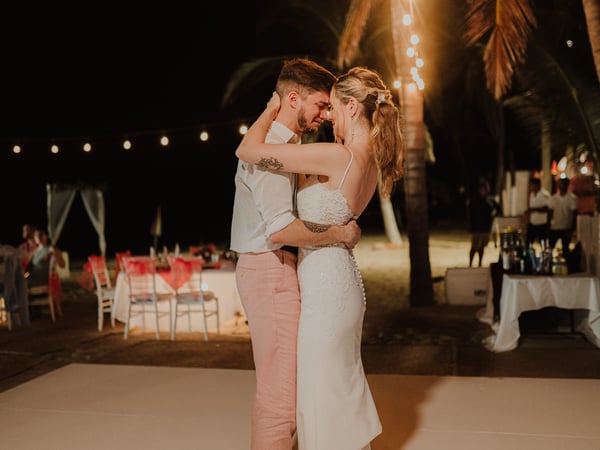 Primer baile de bodas en terraza nocturna con palmeras y luces colgantes frente a la playa