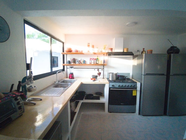 Cocina equipada en L con estufa, refrigerador de acero, repisas de madera y ventana con luz natural