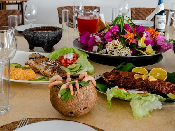 Mesa con platillos de mariscos tropicales: camarones en coco, pescado frito, arroz y flores coloridas como centropieza