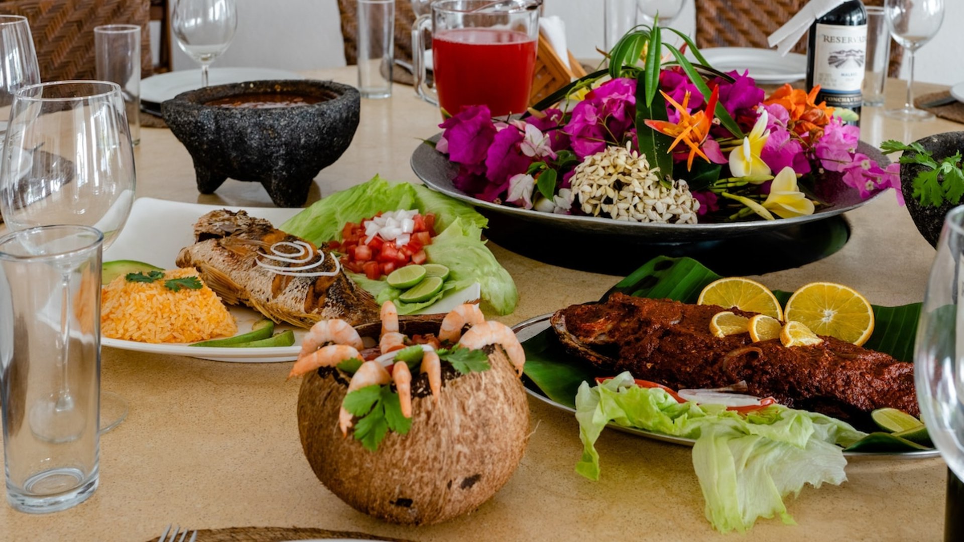 Mesa con platillos de mariscos tropicales: camarones en coco, pescado frito, arroz y flores coloridas como centropieza