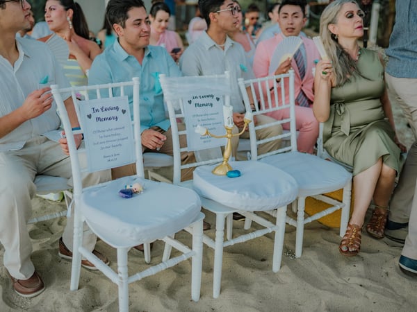 Sillas blancas reservadas con letreros de homenaje en ceremonia de boda en playa con arena