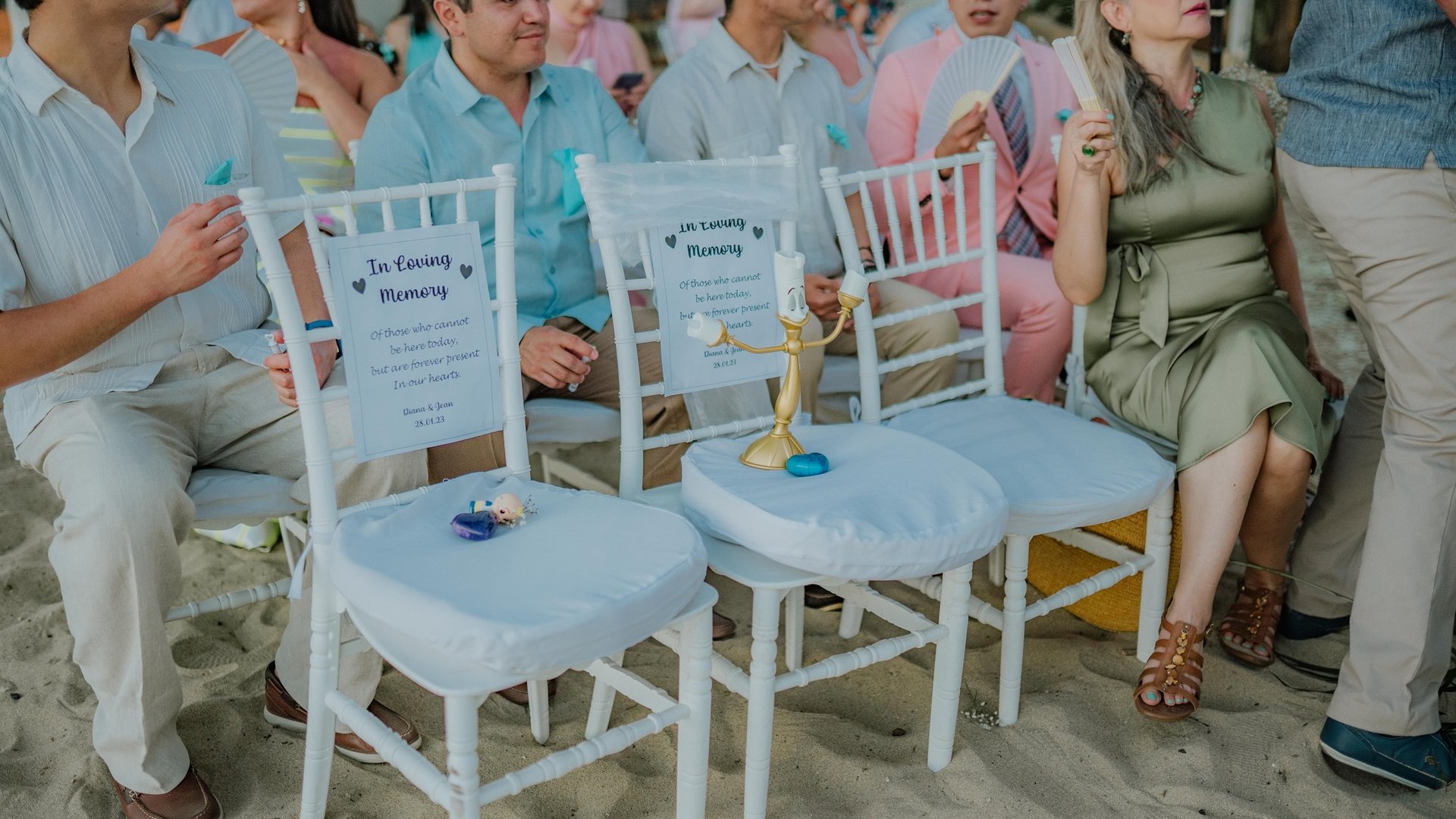 Sillas blancas reservadas con letreros de homenaje en ceremonia de boda en playa con arena