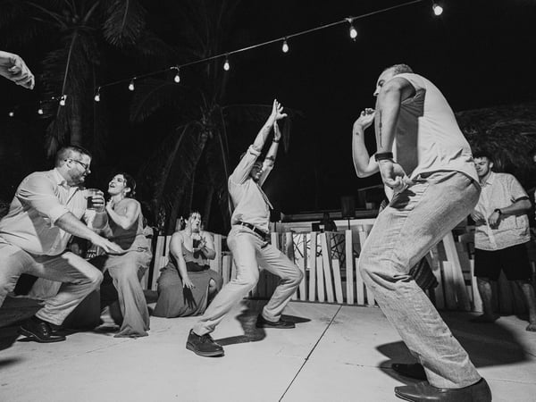 Invitados bailando en pista nocturna con luces colgantes y palmeras en ambiente festivo de boda