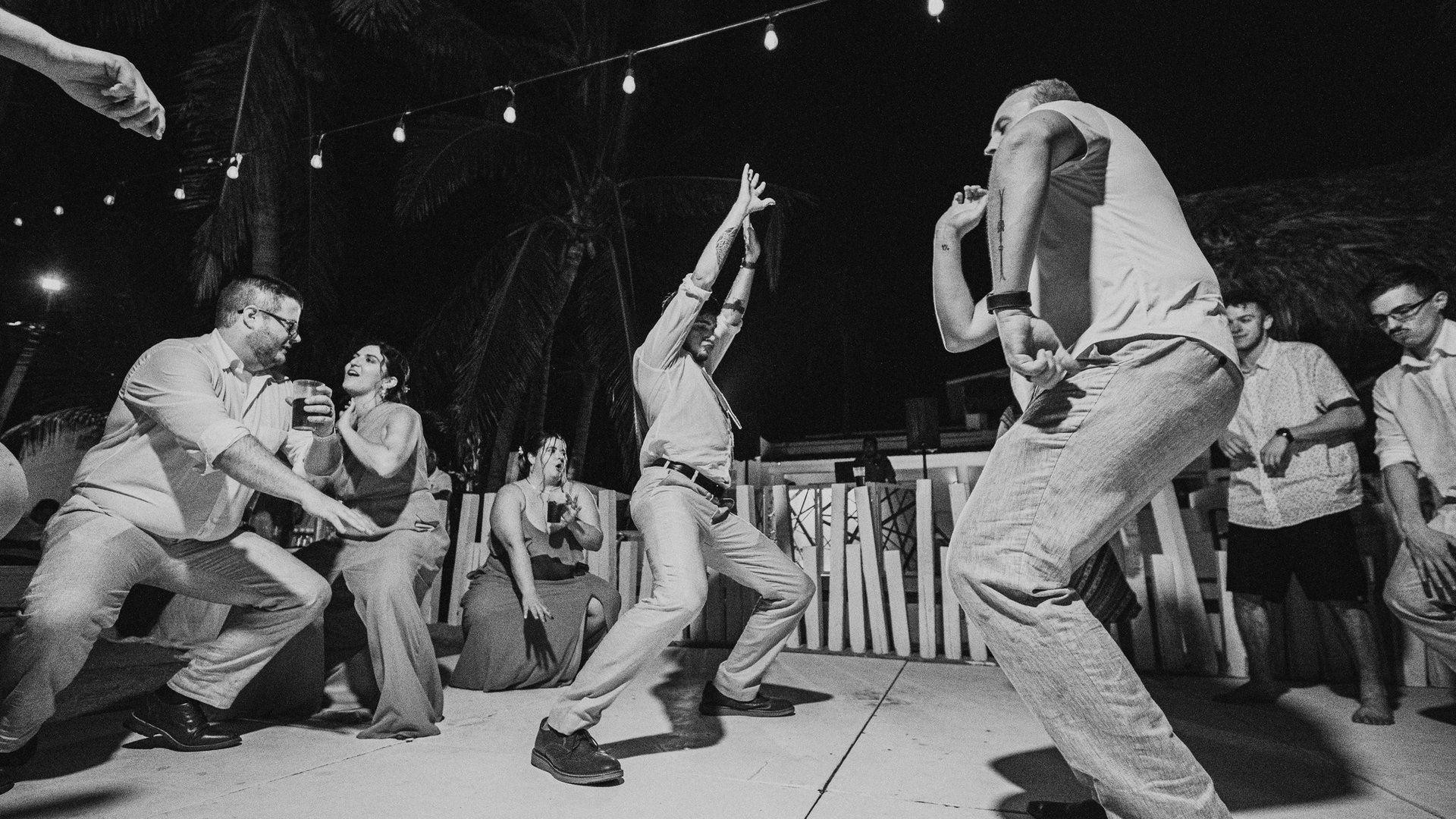 Invitados bailando en pista nocturna con luces colgantes y palmeras en ambiente festivo de boda