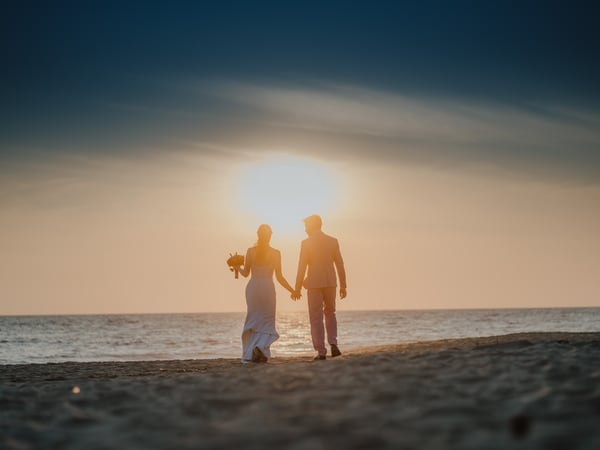 Pareja de recién casados caminando en playa al atardecer frente al mar Pacífico