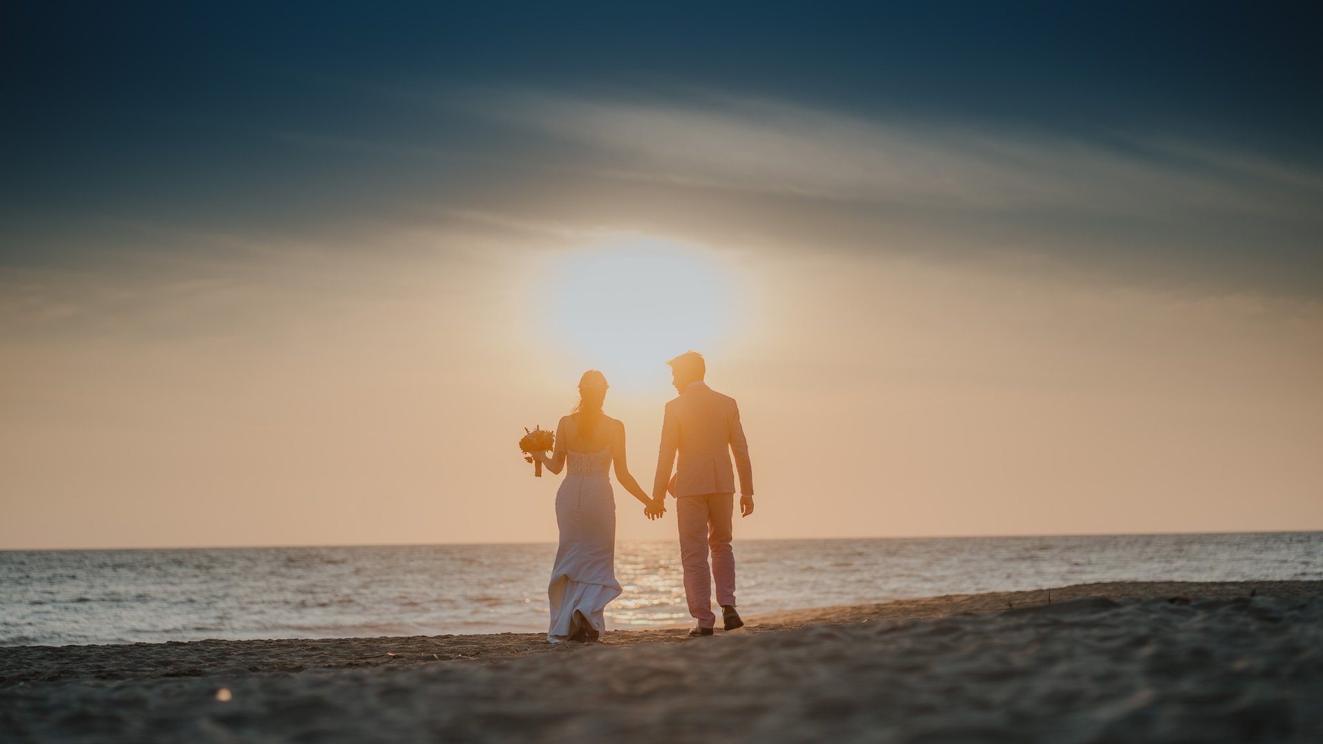 Pareja de recién casados caminando en playa al atardecer frente al mar Pacífico