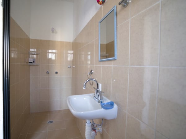 Baño sencillo con azulejos beige, lavabo blanco con llave cromada y espejo de marco azul