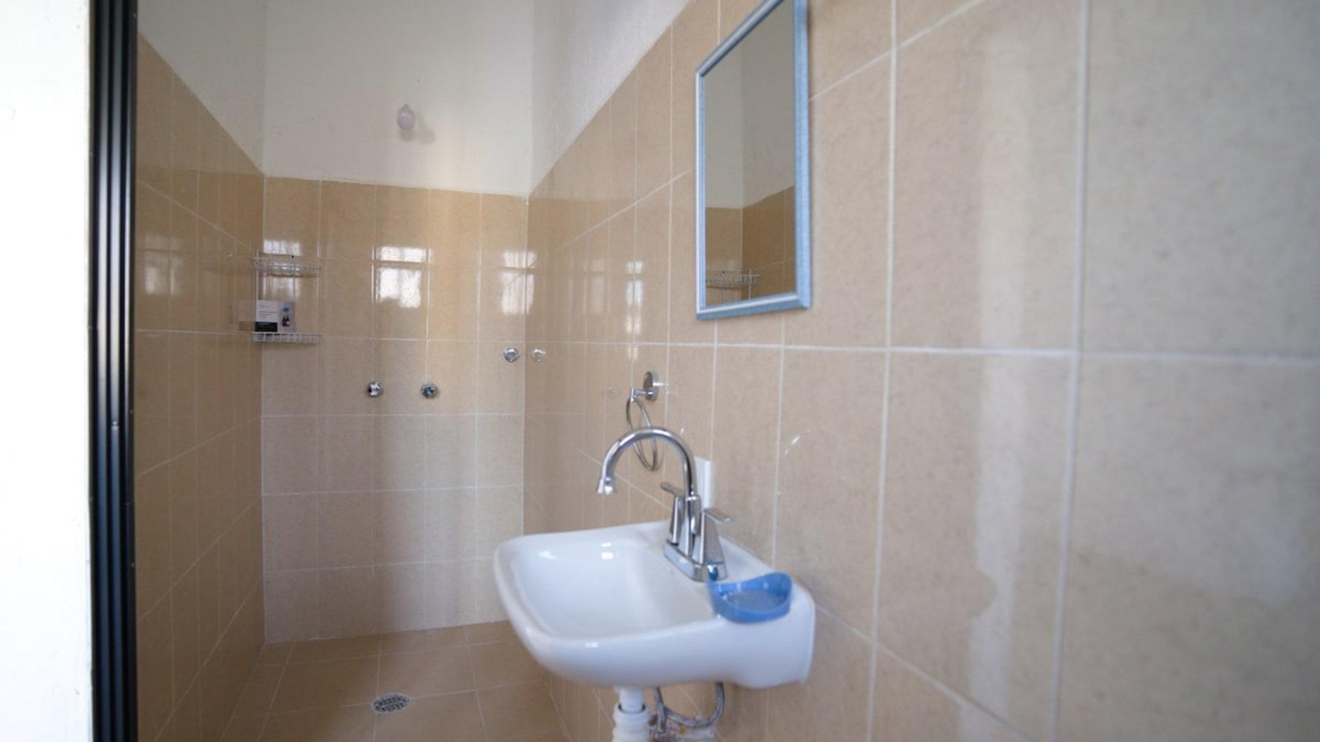 Baño sencillo con azulejos beige, lavabo blanco con llave cromada y espejo de marco azul