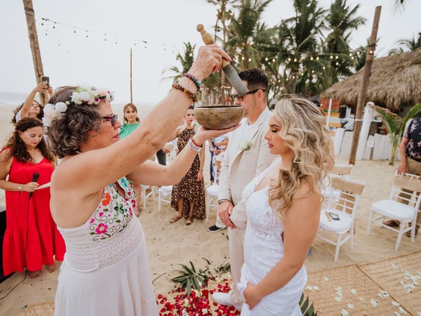 Ritual de ceremonia en playa con palmeras, palapas y luces colgantes al fondo