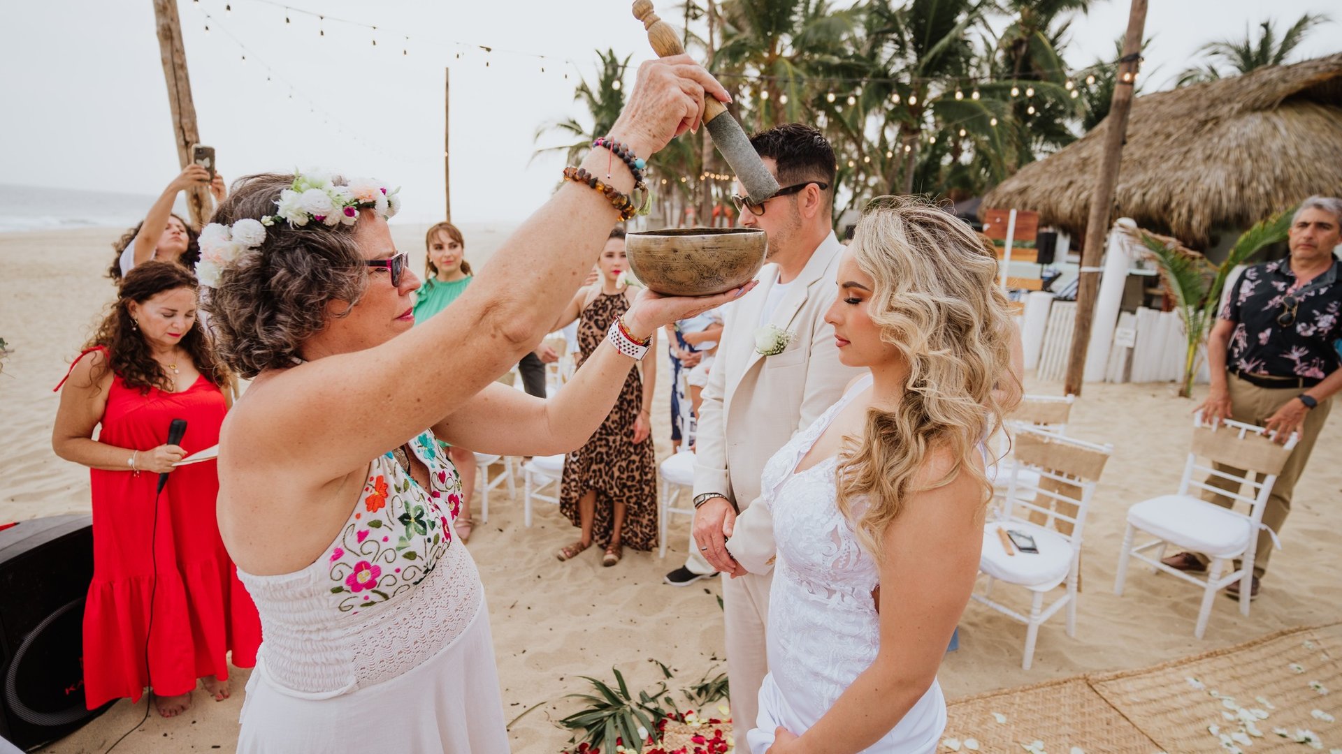 Ritual de ceremonia en playa con palmeras, palapas y luces colgantes al fondo